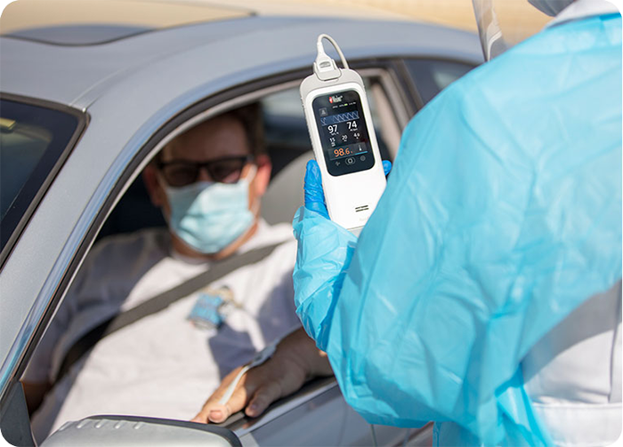 Clinician uses a Masimo Rad-G with Temperature device to check a masked patient’s vitals during drive-through screening.